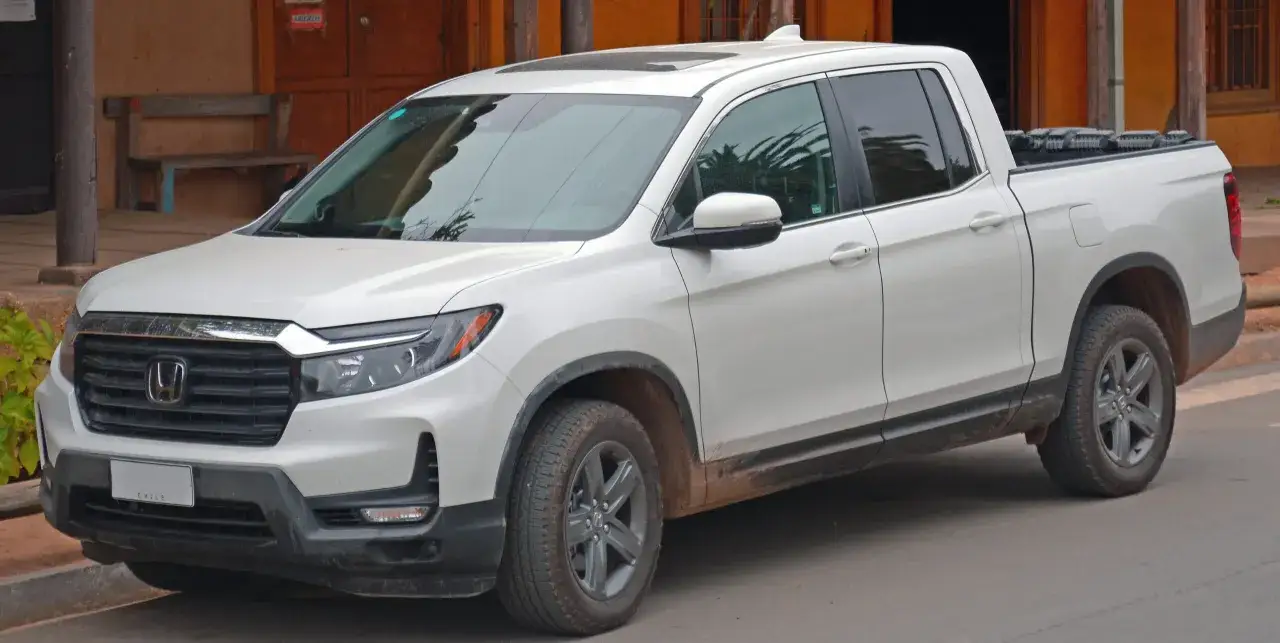 Biały Honda Ridgeline zaparkowany przed budynkiem z drewnianą ławką.
