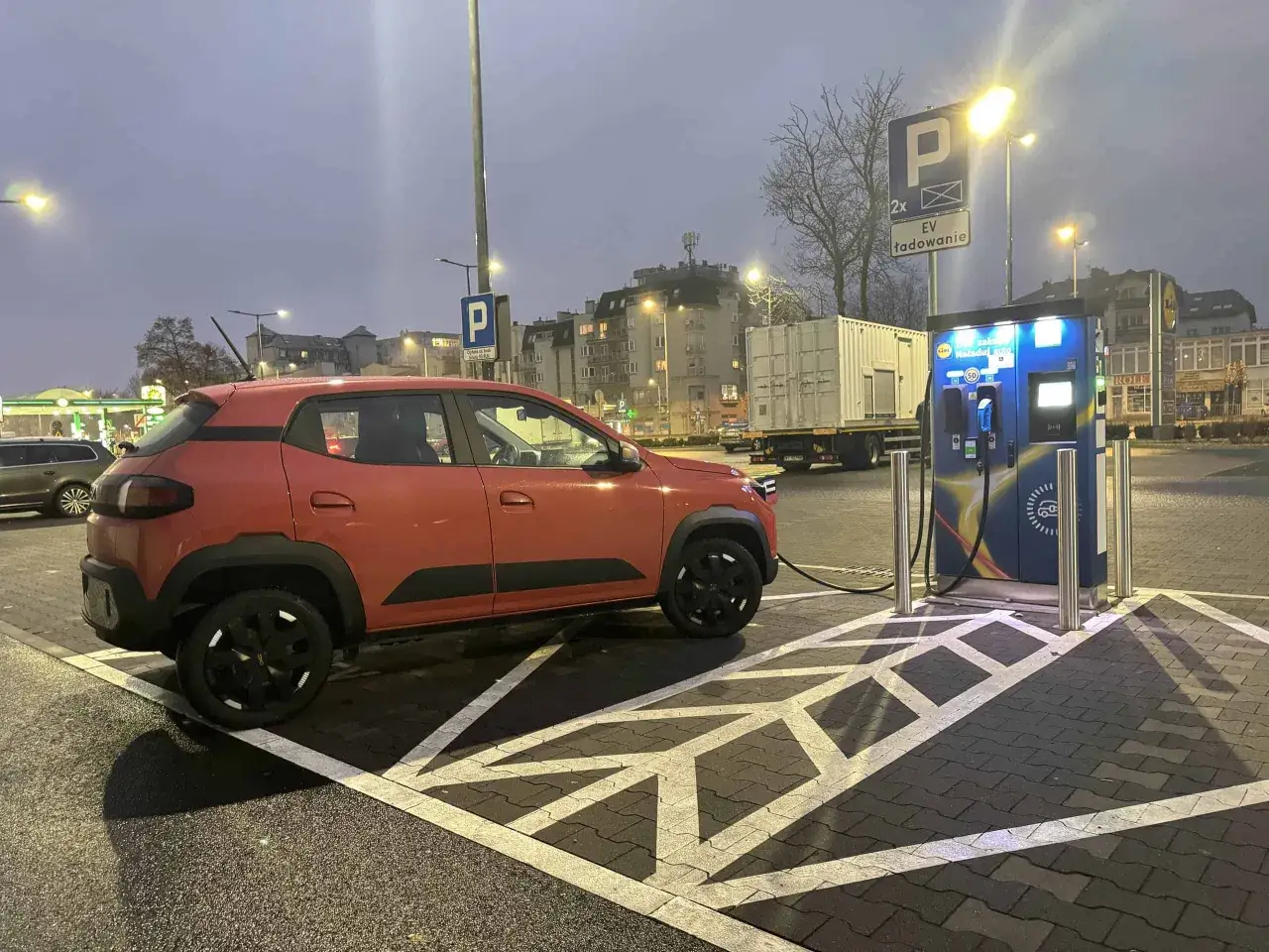 Pomarańczowy Dacia Spring ładuje się na stacji EV. Sprawdź atrakcyjną dacia spring cena!