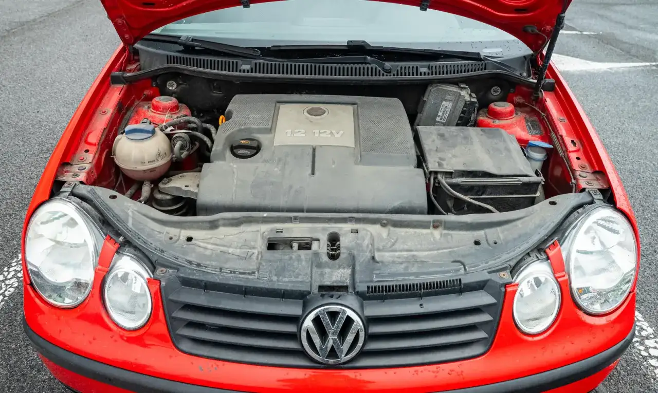Czerwony VW Polo 2010 z otwartą maską, widoczny silnik 1.2 12V i przednie reflektory.