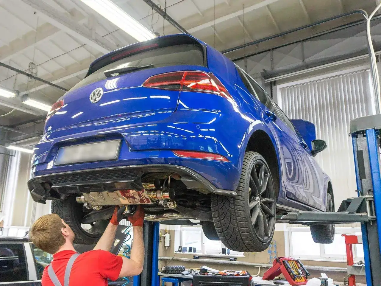 Mechanik pracuje pod niebieskim Volkswagenem na podnośniku. W warsztacie trwa mapowanie silnika, optymalizacja jego pracy.