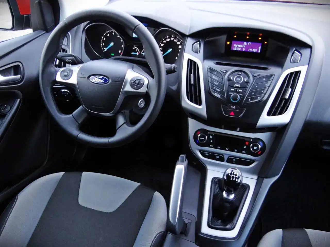 Wnętrze Ford Focus 3: kierownica, deska rozdzielcza z radiem i nawiewami, dźwignia zmiany biegów i siedzenie.