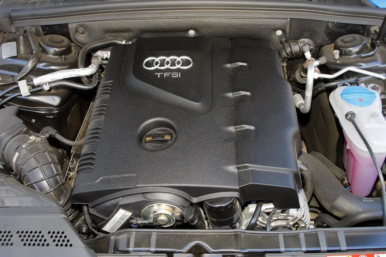 Silnik 2.0 TFSI w Audi A5. Widoczna czarna pokrywa silnika z logo Audi i napisem TFSI, zbiornik płynu chłodniczego.